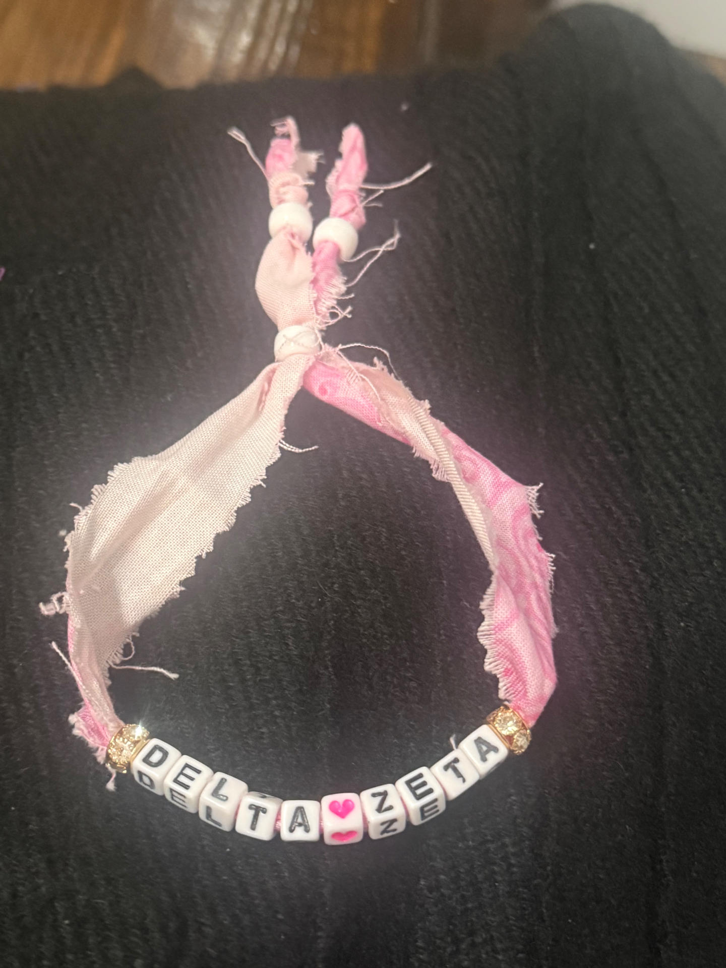 Pink fabric bracelet spelling DELTA heart ZETA with gold sparkle beads