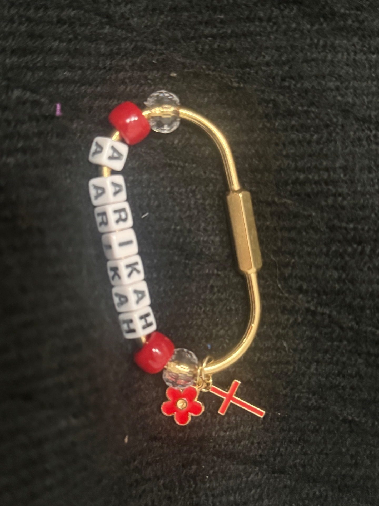 Gold bag clip spelling ARIKAH with red beads, a red flower and a red cross charm