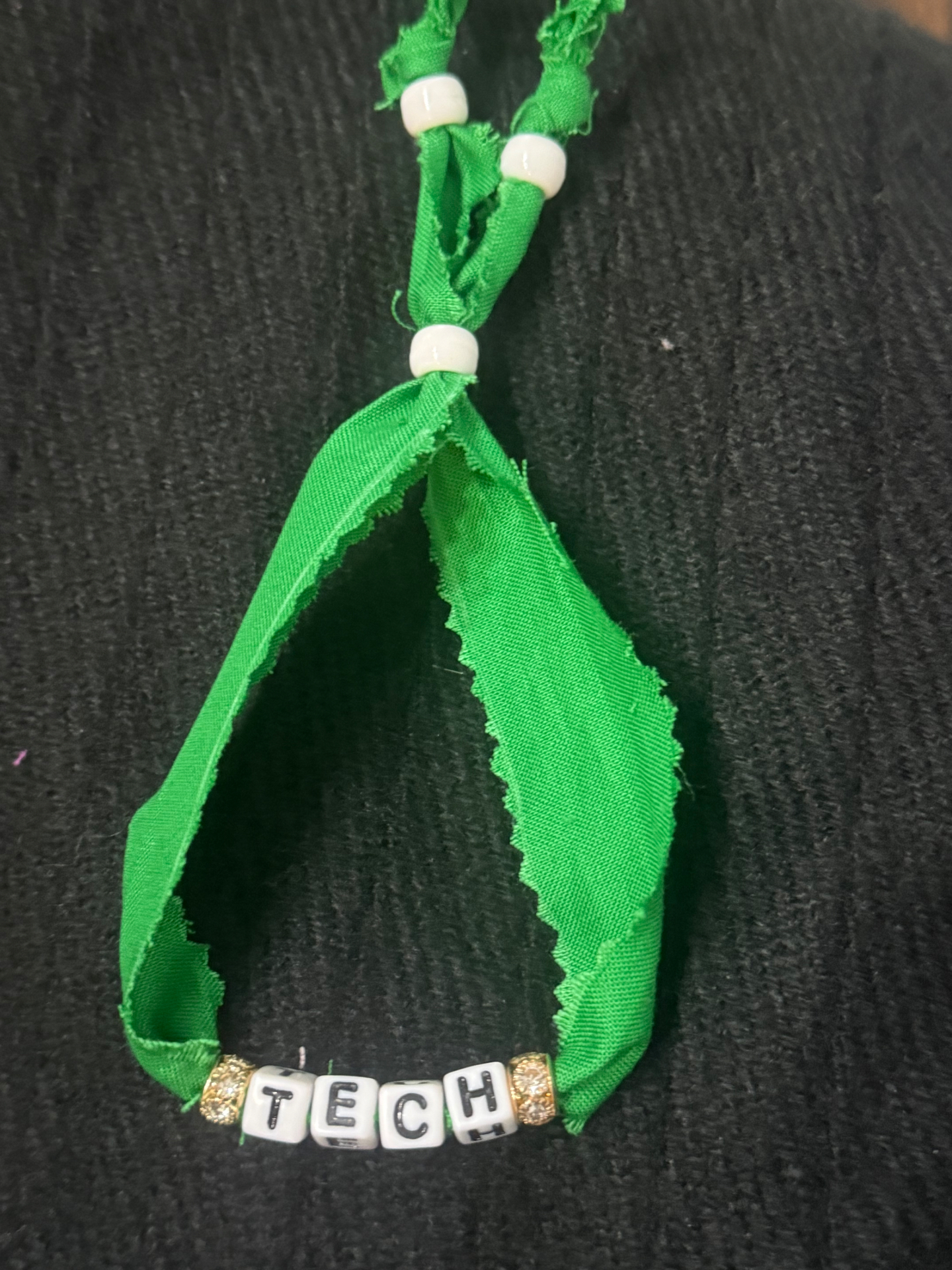 Green fabric bracelet spelling TECH with gold sparkle beads