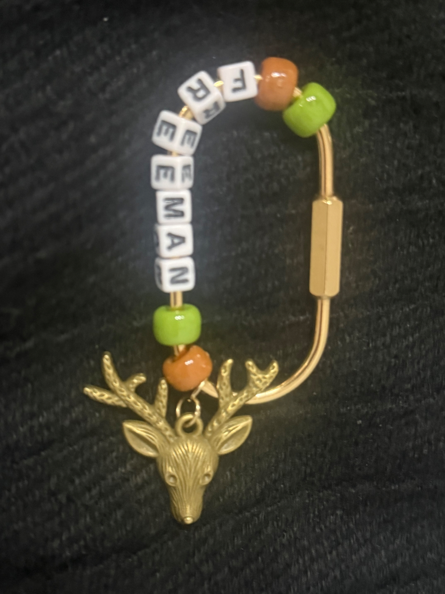 Gold bag clip spelling FREEMAN with green and orange beads and a gold deer charm